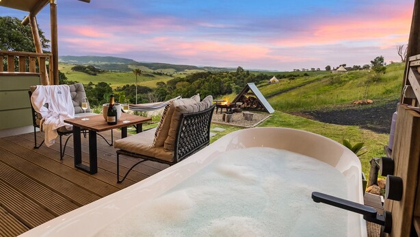 A spa area with a hot tub, seating, and a scenic view of rolling hills. - Cicada Luxury Camping (Jerrara)