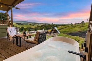 A spa area with a hot tub, seating, and a scenic view of rolling hills. - Cicada Luxury Camping (Jerrara)