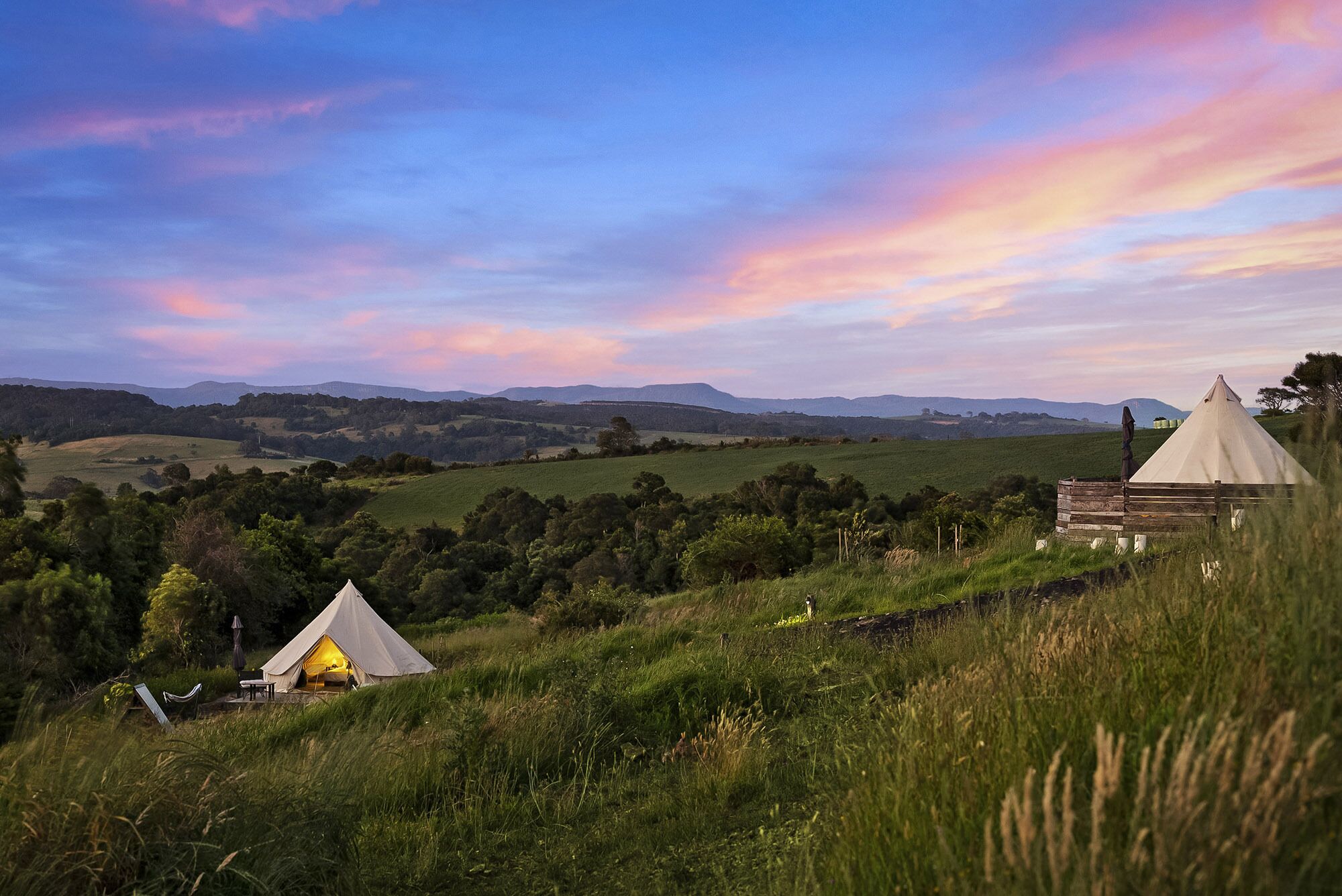A tented accommodation with a view of rolling hills and a sunset sky.