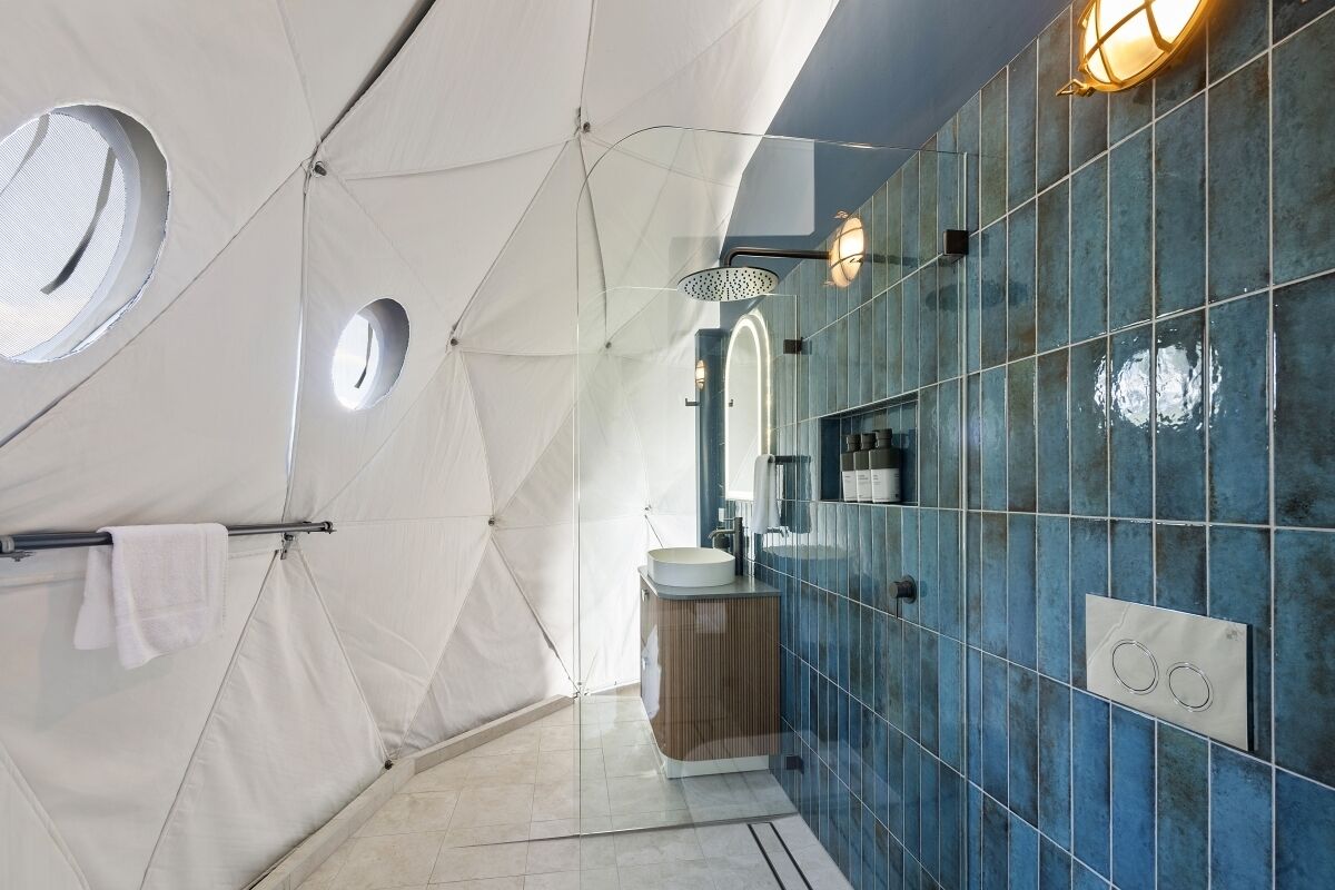 Ein modernes Badezimmer mit einem geometrischen Deckendesign, einem runden Spiegel und blauen Fliesenwänden.