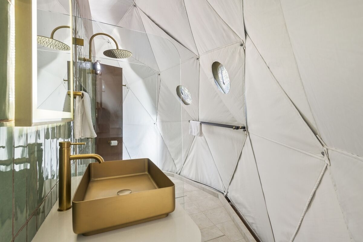 A modern bathroom with a gold sink, a glass shower enclosure, and a white tiled wall.
