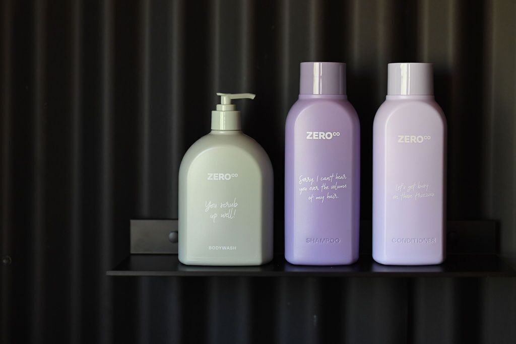 Three ZERO.co bottles on a black shelf against a dark background.