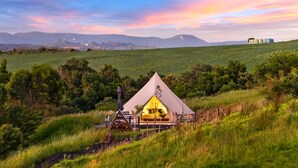 A tented accommodation with a bed and a table, surrounded by greenery and hills. - Cicada Luxury Camping (Jerrara)