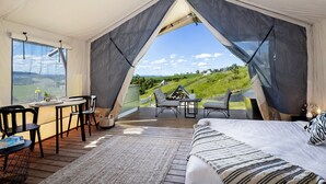 A tented accommodation with a dining area, a bed, and a view of the countryside. - Cicada Luxury Camping (Jerrara)