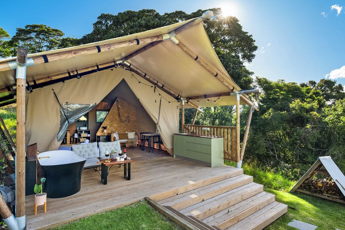 A tented outdoor space with a wooden deck, a dining area, and a kitchen area.