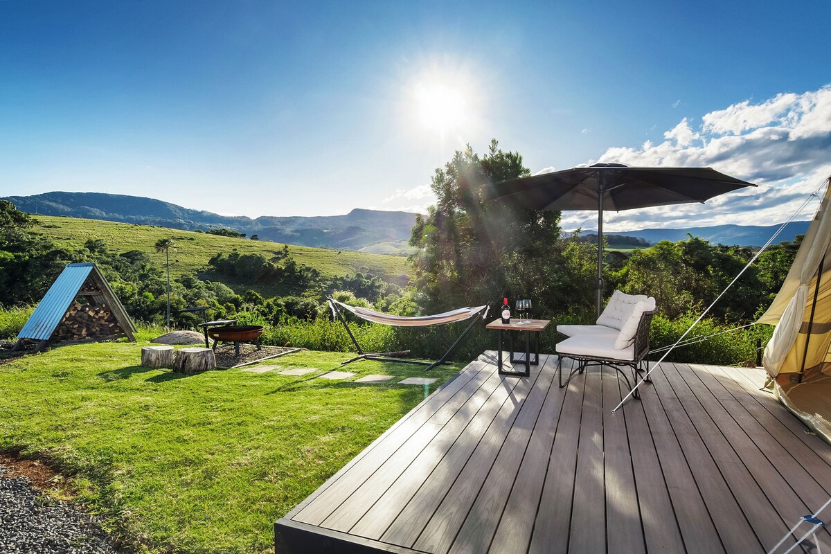 A wooden deck with a hammock, a table with wine glasses, and a tent.