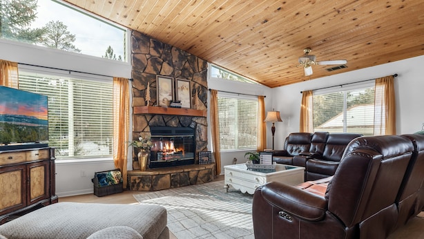 A cozy living room with a stone fireplace, leather recliner, and large windows.