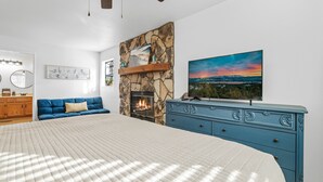 A bedroom with a large bed, a stone fireplace, a blue dresser, and a painting of a sunset.