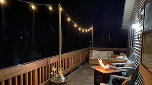 An outdoor deck with a wooden railing, string lights, a fire pit, and a sofa with cushions.