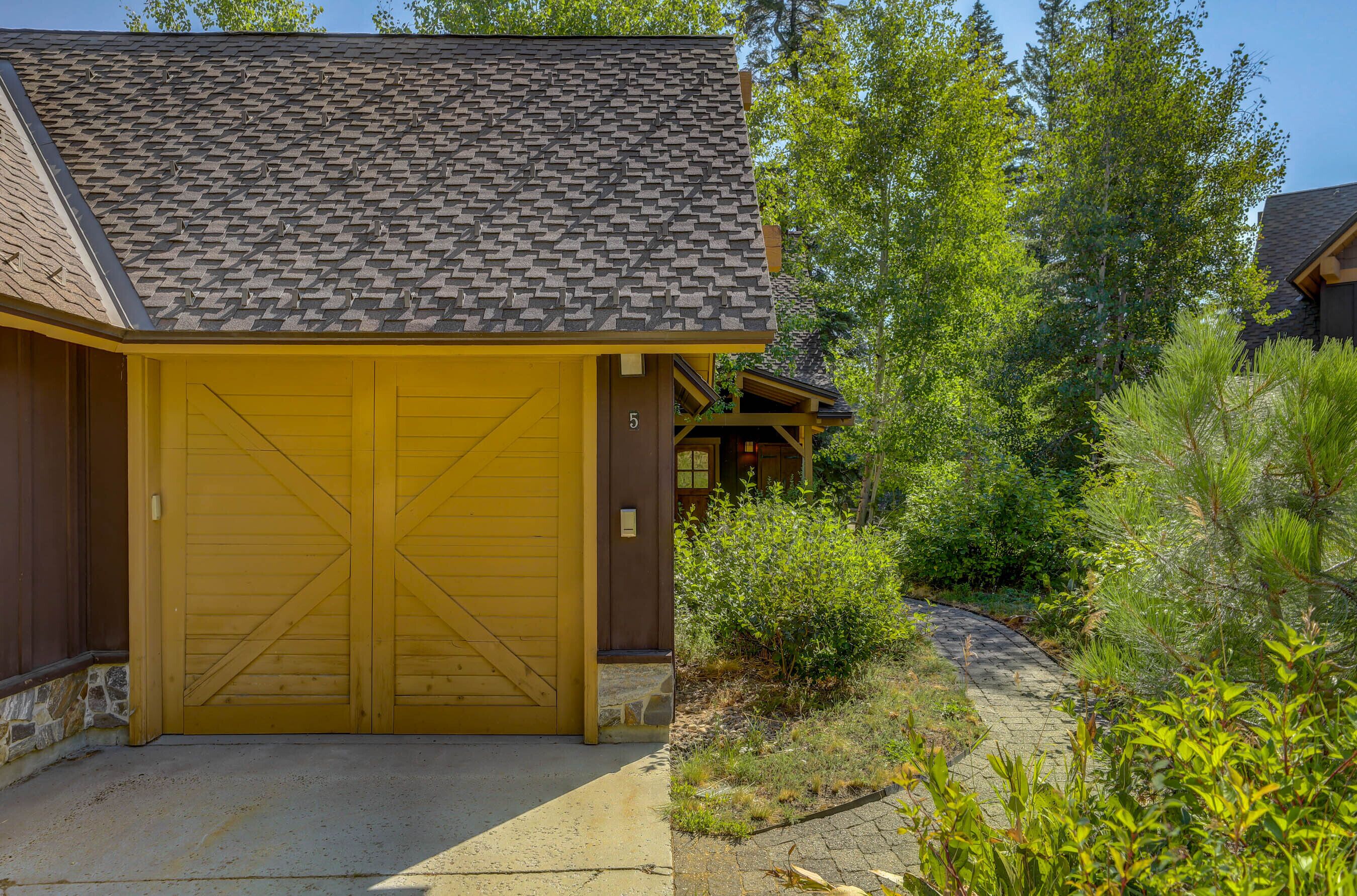 A yellow building with a large garage door, surrounded by greenery and trees.