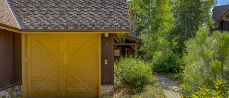 A yellow building with a large garage door, surrounded by greenery and trees.