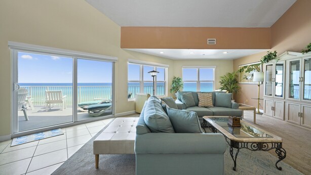 A spacious living room with a large sliding glass door leading to a balcony with a view of the ocean. There is a light blue sofa, a coffee table, and a cabinet with decorative items.