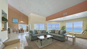 A spacious living room with a large sectional sofa, a coffee table, and a view of the ocean through large windows.