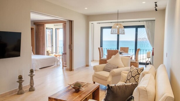 A spacious living area with a sofa, coffee table, and a balcony with a view of the sea. - Casa Del Mar Las Olas Beachfront 2BR Penthouse (San Jose del Cabo)