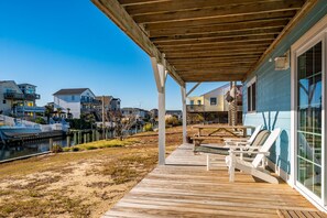 Une terrasse en bois avec des chaises longues, une vue sur un plan d’eau et des maisons en arrière-plan.