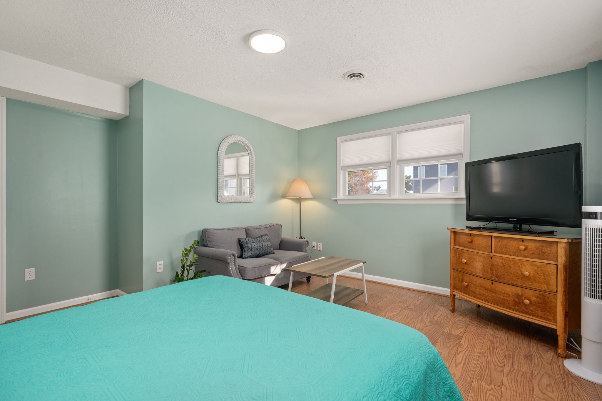 A bedroom with a bed, a sofa, a TV, a dresser, and a lamp.