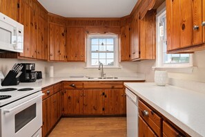 Une cuisine avec des meubles de rangement en bois, un fourneau blanc, un évier et une fenêtre au-dessus de l’évier.