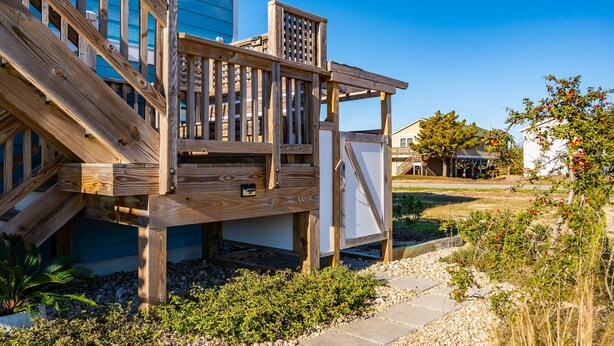 Une terrasse en bois avec un escalier menant à une zone abritée, entourée de gravier et de plantes.