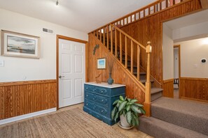 Un escalier avec des rampes en bois et des marches recouvertes de moquette, une commode bleue avec des tiroirs, une plante en pot et un tableau encadré accroché au mur.