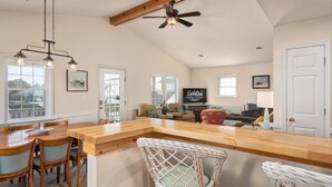 Un vaste espace de vie comprenant une table à manger en bois, des chaises en osier, un ventilateur de plafond et un téléviseur.