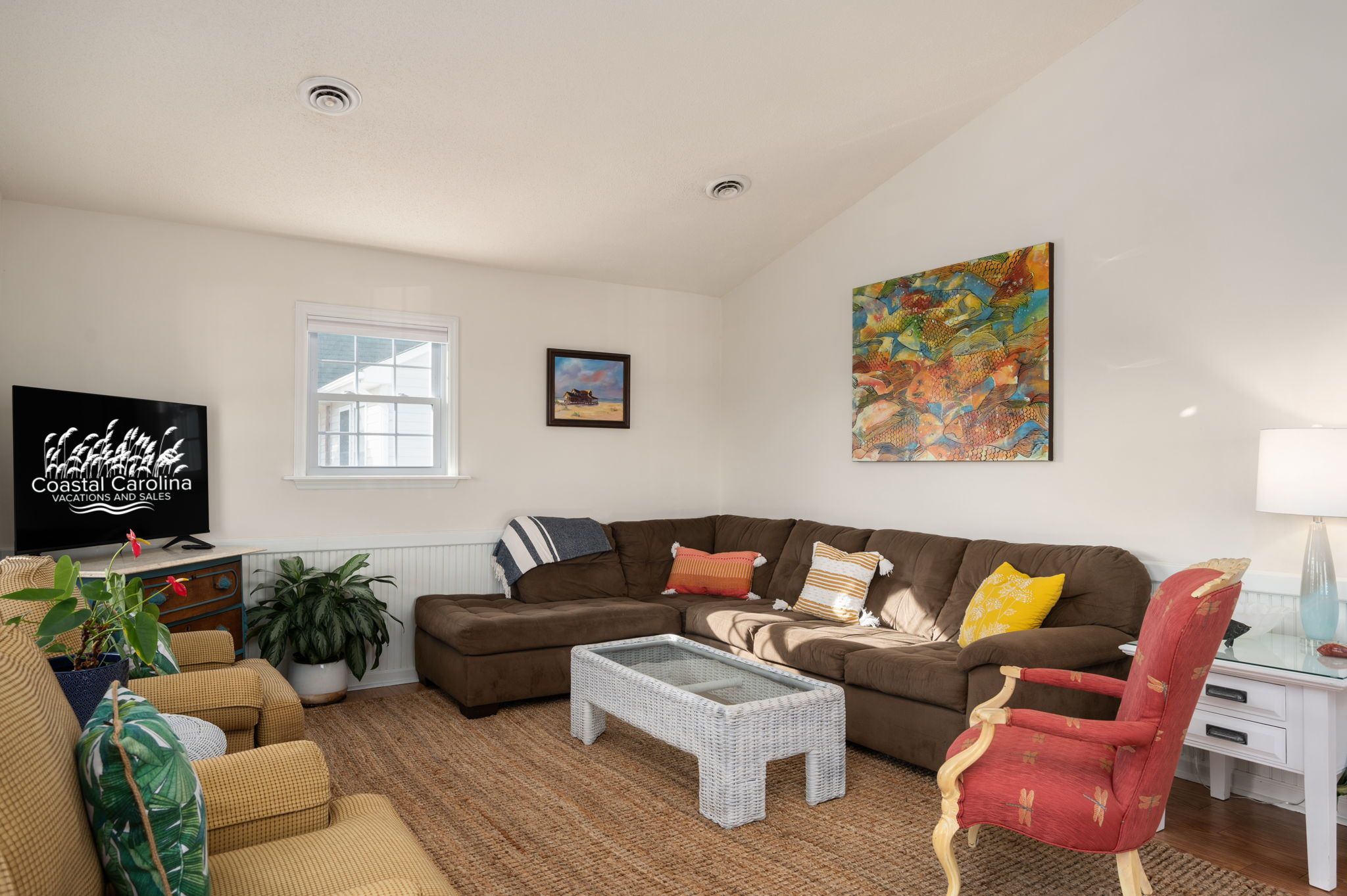 A living room with a brown sofa, a glass coffee table, a red chair, a TV, and a painting on the wall.