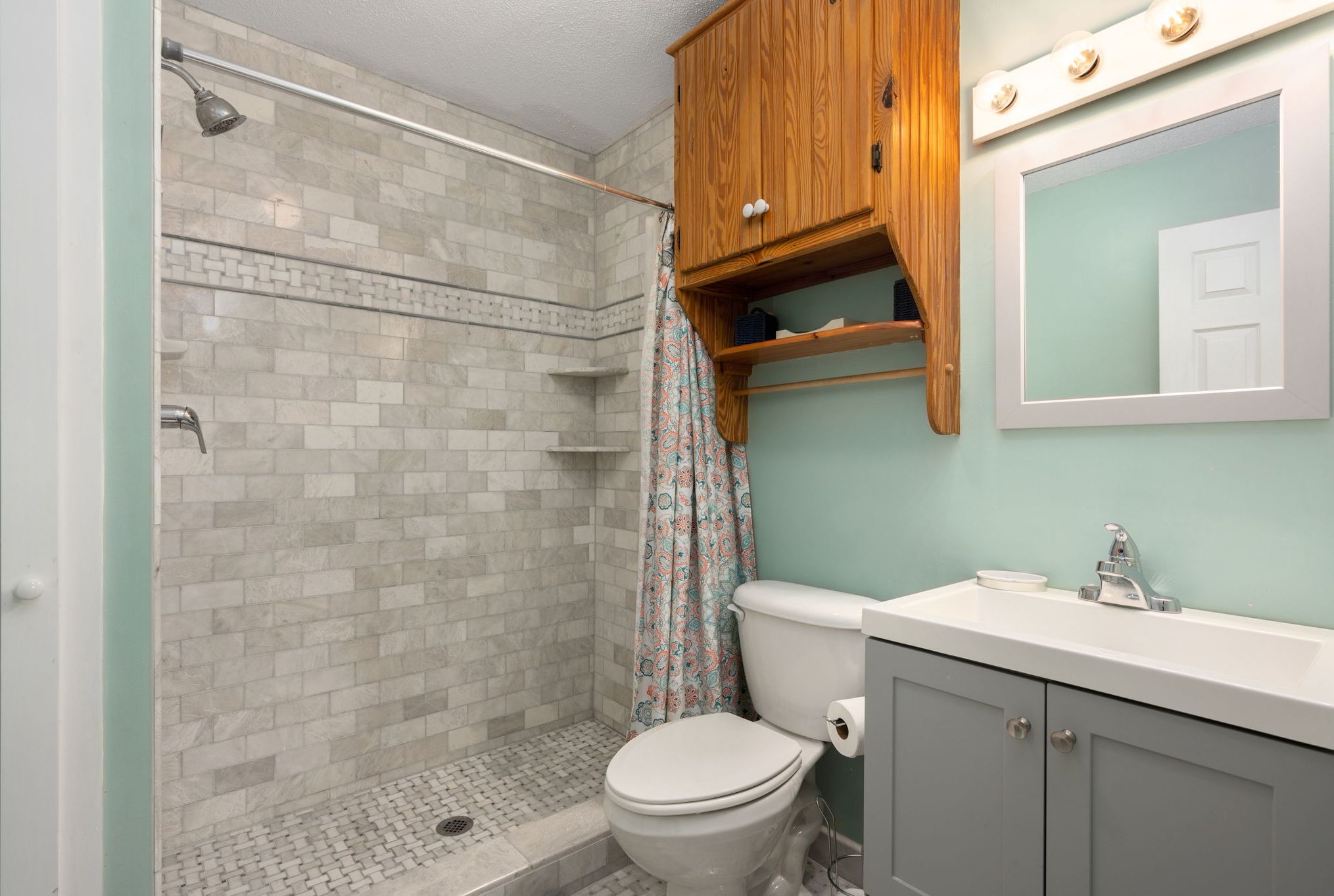 A bathroom with a shower, toilet, vanity, and a mirror.