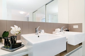 A modern bathroom with two sinks, a large mirror, and a small orchid plant.