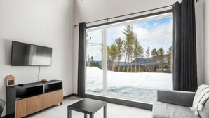 Un salon moderne doté d’une grande fenêtre, d’un téléviseur à écran plat, d’un meuble en bois et d’un canapé gris.