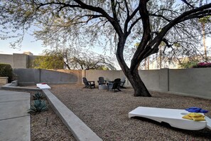 Un espacio al aire libre con sillas Adirondack y una silla lounge blanca, rodeado de grava y un árbol.