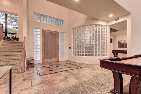 Un interior espacioso con escalera, mesa de billar y un amplio ventanal con un panel decorativo.