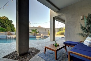 A poolside area with a lounge chair, a small table with a bottle and bowl, and a string of lights.