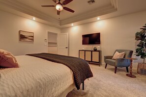 A bedroom with a bed, a chair, a television, and a ceiling fan.