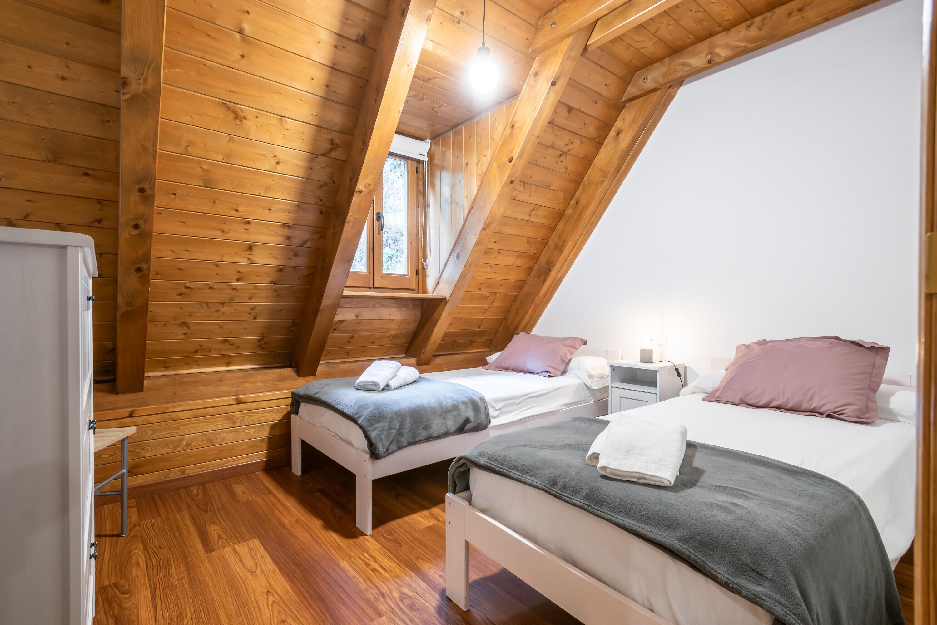 Une petite pièce chaleureuse aux murs en bois et au plafond en pente, comprenant deux lits et une petite table.
