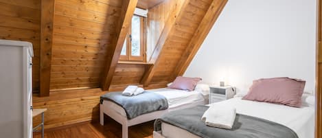 Une petite pièce chaleureuse aux murs en bois et au plafond en pente, comprenant deux lits et une petite table.