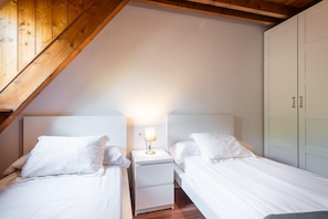 A bedroom with two beds, a nightstand with a lamp, and a wardrobe.