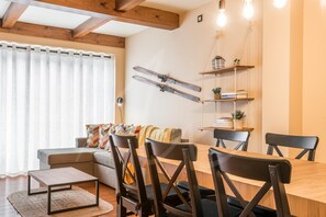 A cozy living room with a wooden dining table, chairs, a sofa, and a ski rack on the wall.