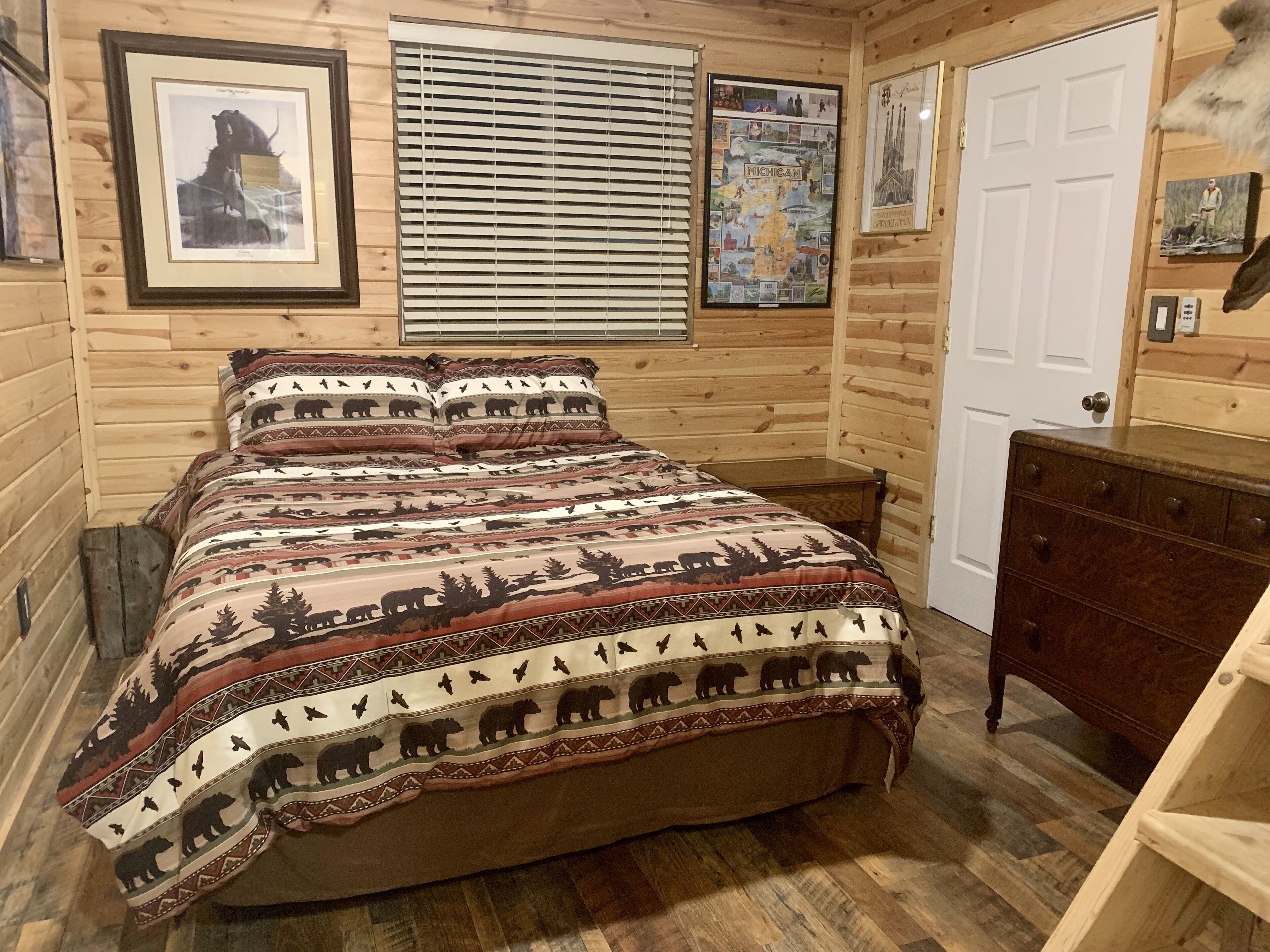 Une chambre dans une cabane en bois, avec un lit, une commode et un mur décoré de tableaux encadrés.