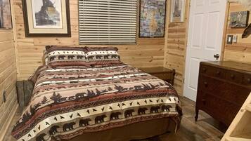 Une chambre dans une cabane en bois, avec un lit, une commode et un mur décoré de tableaux encadrés.