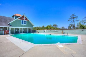 Ein rechteckiger Swimmingpool mit einer Betonplattform, ein überdachter Bereich mit Gründach und ein Gebäude mit rotem Dach und weißer Fassade.