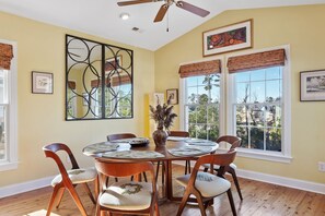 Comedor con una mesa redonda, seis sillas, ventilador de techo y ventanas amplias con vistas al exterior.