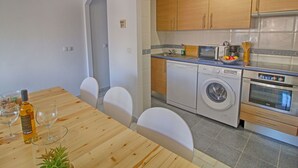 A modern kitchen with wooden cabinets, a washing machine, a microwave, and a dining area with a wooden table and chairs.