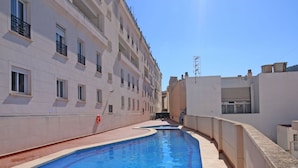A swimming pool with a curved edge, adjacent to a multi-story building with balconies and windows.