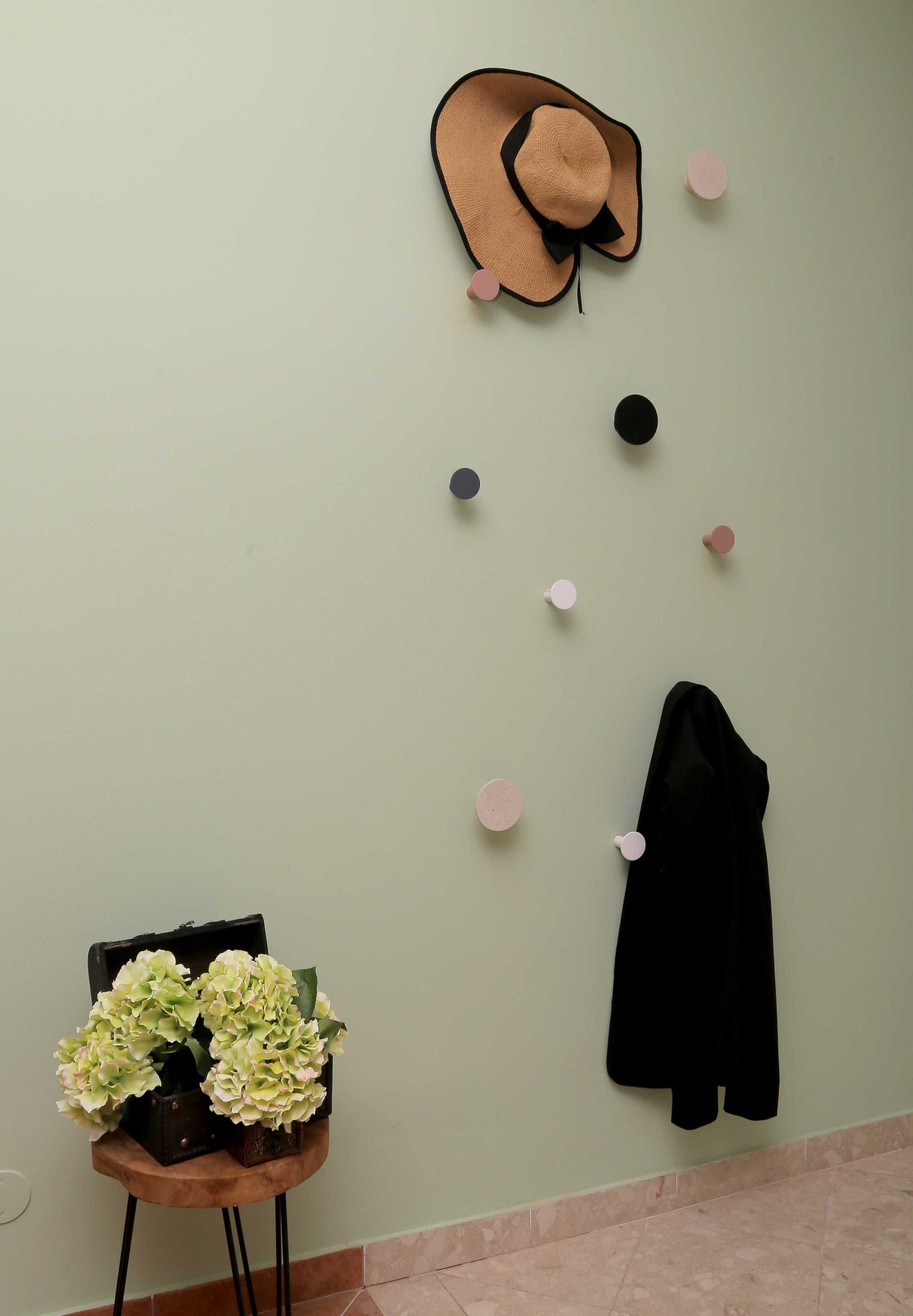 Eine Wand mit Hut, verstreuten dekorativen Kreisen, einer schwarzen Jacke und einem kleinen Tisch mit künstlichen Blumen.