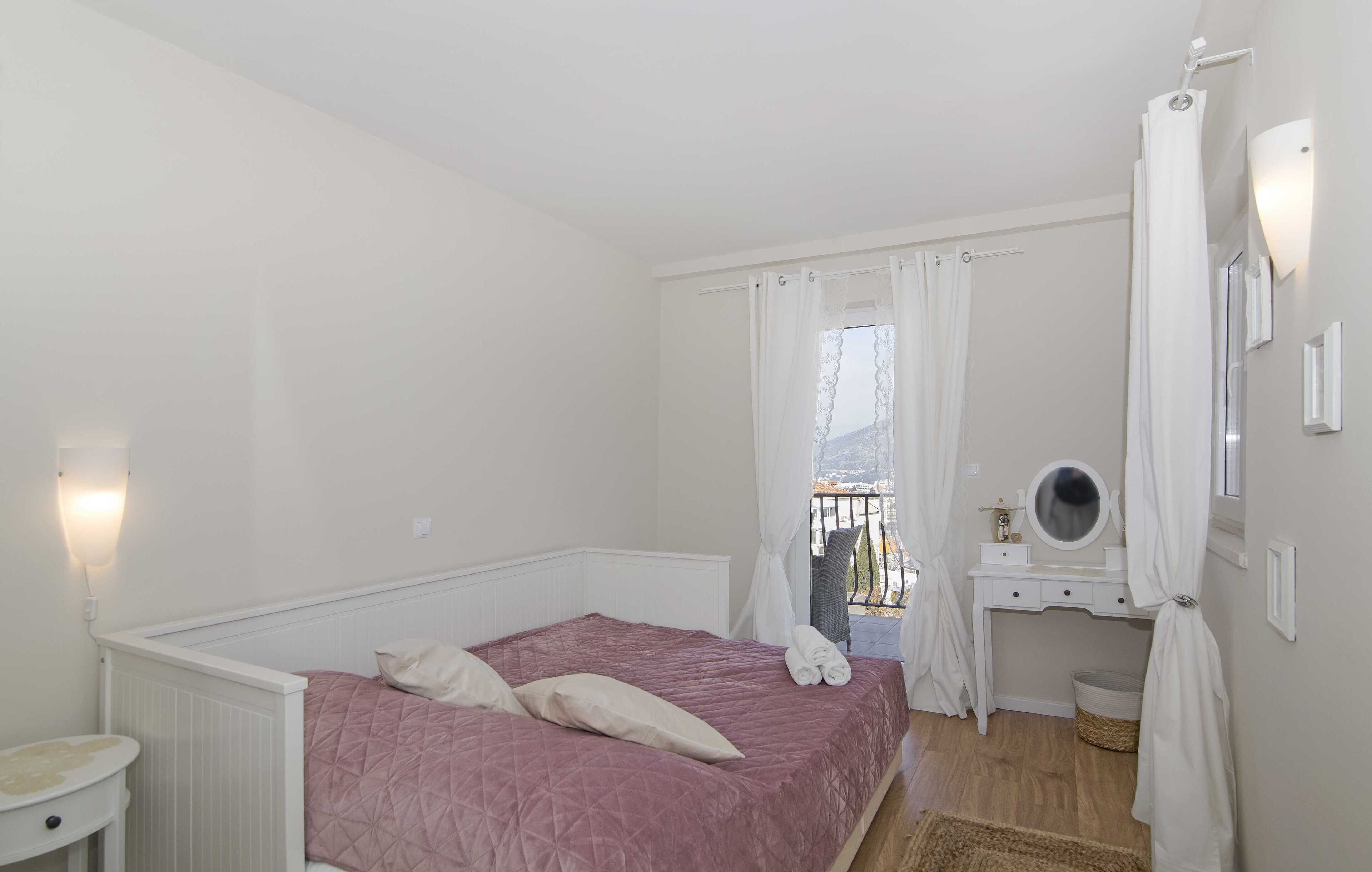 Une chambre à coucher avec un lit, une table de chevet, un miroir et une fenêtre avec des rideaux.