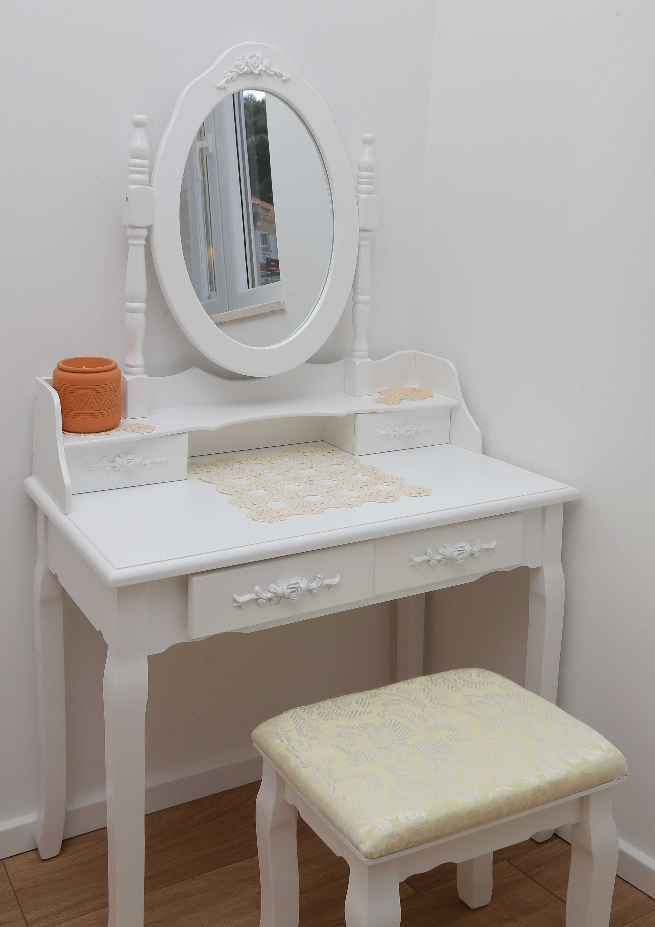 A white vanity with a mirror, drawers, and a stool.