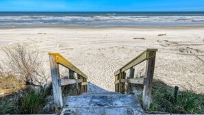 Una escalera de madera que baja a una playa arenosa, con el océano al fondo.