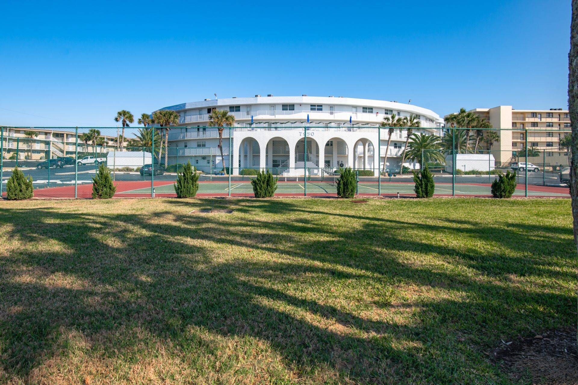 A large, white, circular building with arched windows, surrounded by a fence and palm trees.
