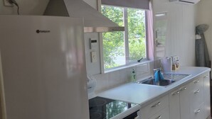 A modern kitchen with white cabinets, a built-in oven, a stainless steel sink, and a window with a view of greenery outside. - The Pink House (Tokoroa)