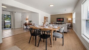 Una sala moderna con una mesa de comedor de madera dispuesta para cuatro personas, un sofá, una mesa de centro y un letrero de Netflix en la pared.