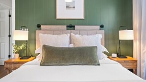 Una cama bien hecha con un cojín verde, dos lámparas de noche y un cuadro en la pared.